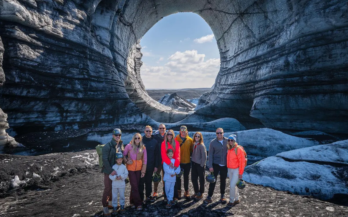 A group of about ten people standing under the round mouth of an ice cave with daylight behind them