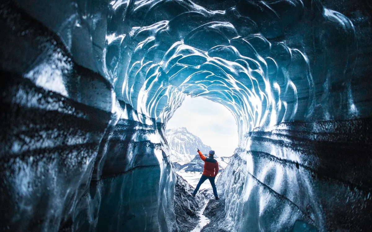 A visitor standing in a round tunnel of ribbed blue ice with daylight behind them