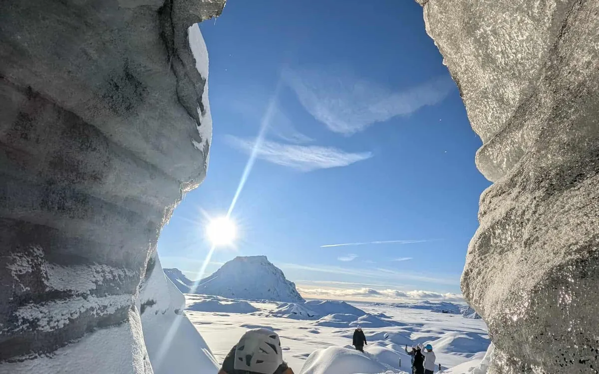 Sunlight flaring between two tall grey ice walls with walkers far below