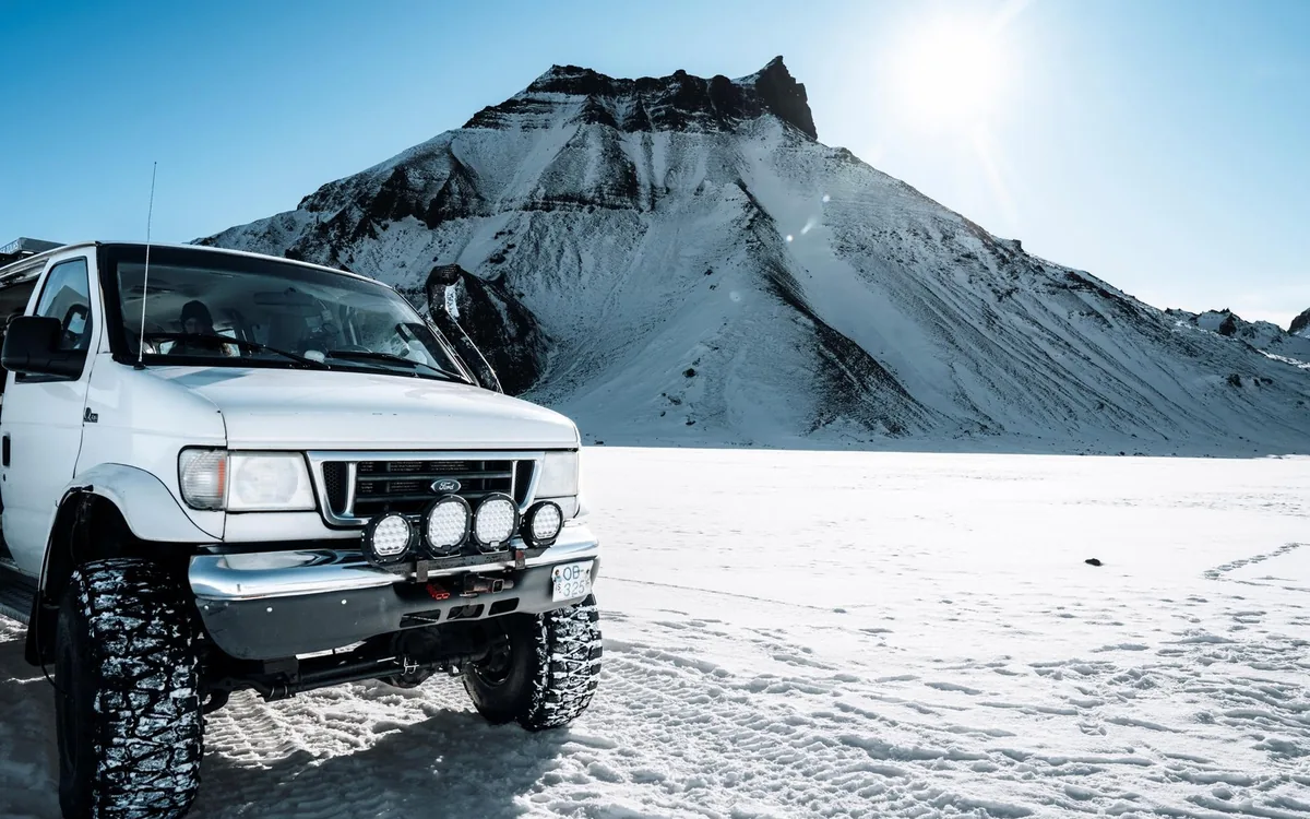 A white four-wheel drive with oversized tyres parked on snow below a snow-covered mountain
