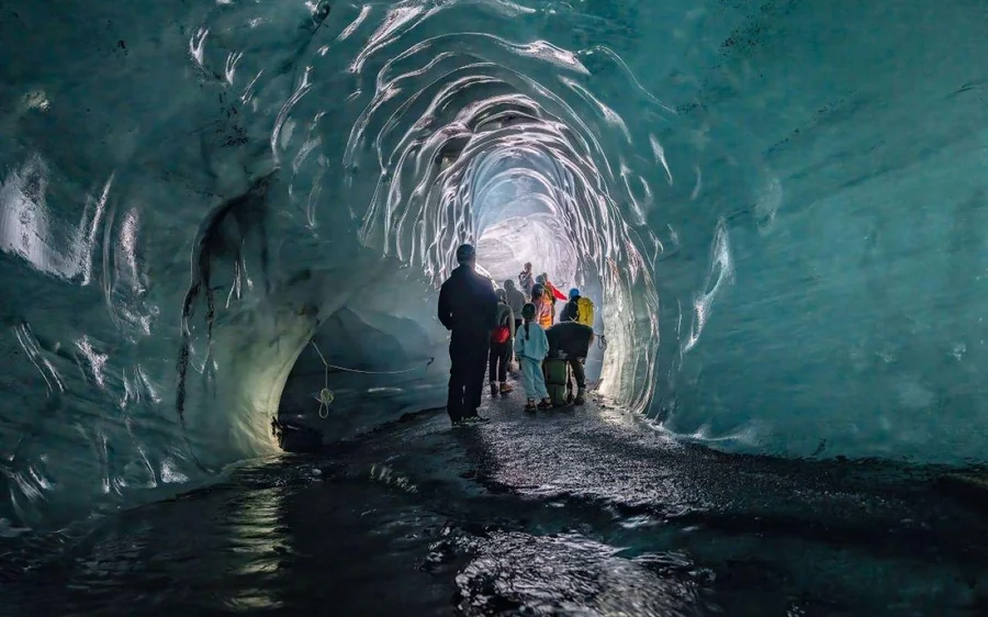 A group walking into a dark blue ice cave towards a bright opening