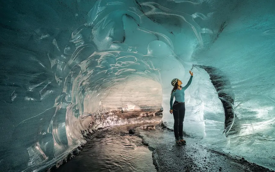 A woman standing in a blue-grey ice cave with dark ash layers running through the walls