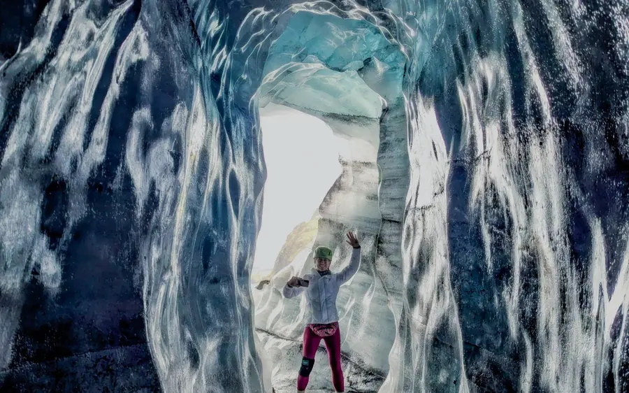 A small figure between tall grey ribbed ice walls deep inside a cave