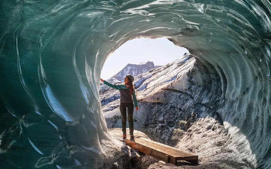 A figure standing on a wooden plank at a round cave mouth that opens onto snowy mountains