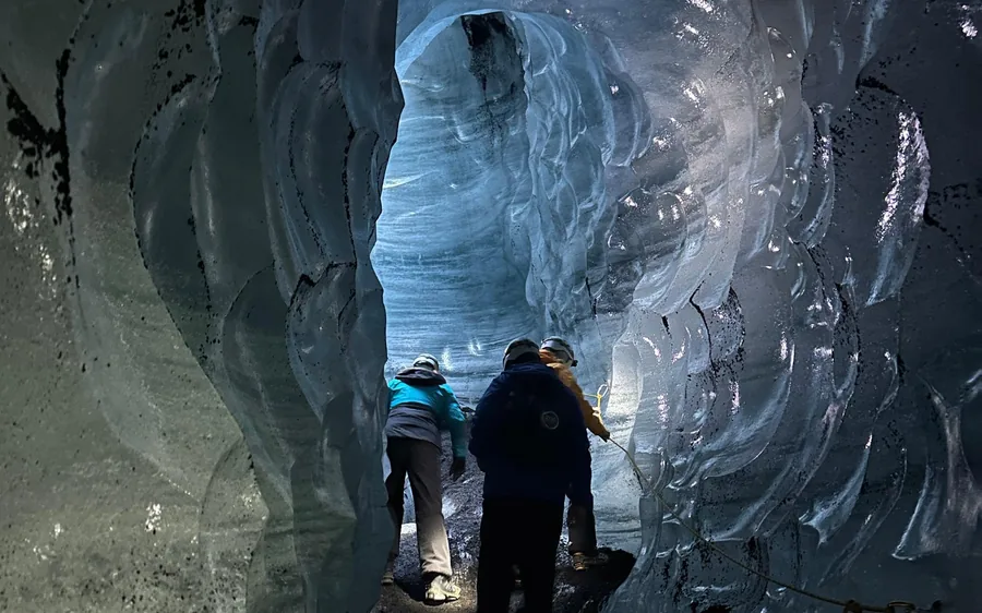 Visitors standing inside a dark ice cavern with blue walls above them