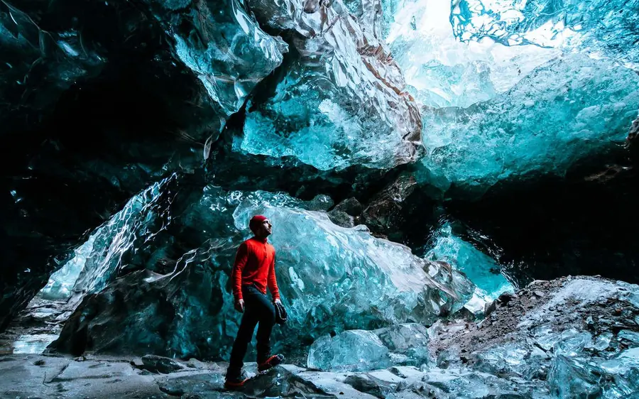 A walker in a red jacket standing deep inside a blue ice cavern